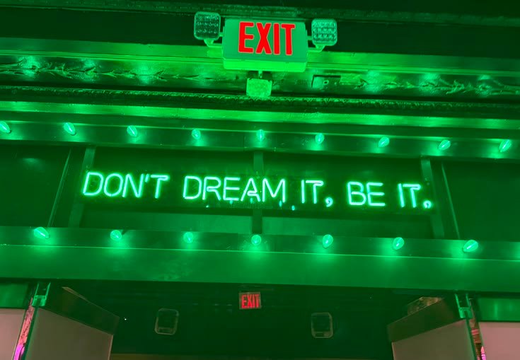 A green neon sign: Don't dream it, be it